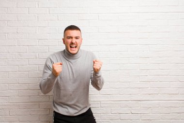 Genç yakışıklı adam sinirli, sinirli, sinirli bakışlar ve sıkı yumruklarla bağırıyor, düz arkaplana karşı öfkeli hissediyor.