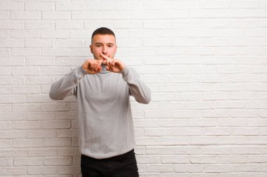 Genç ve yakışıklı bir adam ciddi görünüyor ve iki parmağının önde olması hoşnutsuzca reddedilerek düz arkaplan karşısında sessizlik istiyor.