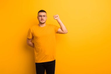 Genç yakışıklı adam kendini ciddi, güçlü ve isyankar hissediyor, yumruğunu kaldırıyor, düz arkaplana karşı devrim için protesto ediyor ya da savaşıyor.