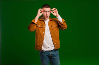 Genç yakışıklı adam şaşkın, şaşırmış ve şaşırmış hissediyor. Elinde hayret dolu, inançsız bir bakışla düz arkaplana bakıyor.