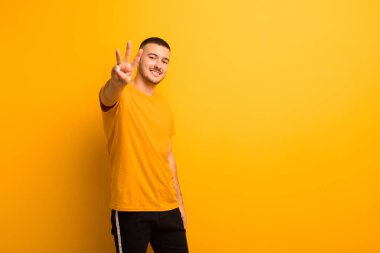 Genç yakışıklı adam gülümsüyor ve arkadaş canlısı görünüyor. Üç ya da üç numarayı gösteriyor. Elleri önde, düz arkaplanda geriye doğru sayıyor.