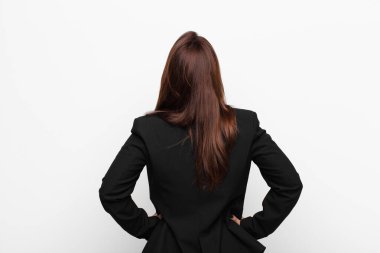 Genç, güzel iş kadını kafası karışık ya da dolu hissediyor ya da şüphe ve sorular, merak ediyor, elleri kalçasında, beyaz duvara karşı dikiz manzaralı