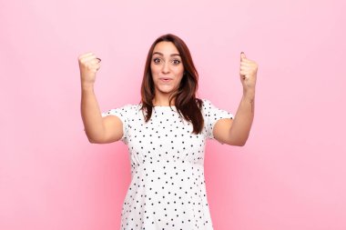 Genç ve güzel bir kadın inanılmaz bir başarıyı kutluyor. Kazanan gibi, heyecanlı ve mutlu görünüyor. Al bakalım! Pembe duvara yaslan