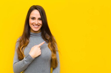 Genç, güzel bir kadın neşeyle gülümsüyor, mutlu hissediyor ve yan ve yukarı doğru işaret ediyor, fotokopi işi veya iş konseptinde nesne gösteriyor.