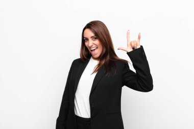 Genç, güzel iş kadını kendini mutlu, eğlenceli, kendinden emin, pozitif ve asi hissediyor, beyaz duvara yaslanmış kaya ya da ağır metal işareti yapıyor.