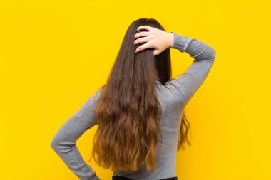 Genç güzel bir kadın düşünüyor ya da şüphe ediyor, kafasını kaşıyor, kafası karışık ve şaşkın hissediyor, arka ya da arka plan işi ya da iş konsepti