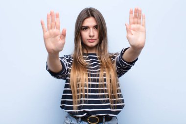 Genç ve güzel bir kadın ciddi, mutsuz, kızgın ve hoşnutsuz görünüyor. Ya da her iki avuç içi açık şekilde, yumuşak mavi duvara yaslanarak durmanı söylüyor.