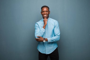 Genç Afro-Amerikan siyahi adam mutlu görünüyor ve gülümsüyor. Elleri çenesinde, merak ediyor ya da soru soruyor. Seçenekleri karşılaştırıyor.