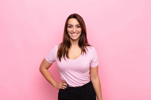 ピンクの壁に対して自信を持って前向きな誇りと友好的な態度で喜んで笑顔若いかなりの女性 — ストック写真