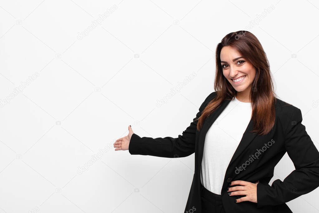 young pretty businesswoman feeling happy and cheerful, smiling and welcoming you, inviting you in with a friendly gesture against white wall