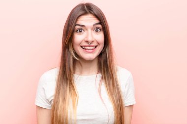 Genç, güzel bir kadın mutlu ve hoş bir şekilde şaşırmış görünüyor. Pembe duvarın karşısında büyüleyici ve şok olmuş bir ifade karşısında heyecanlanıyor.