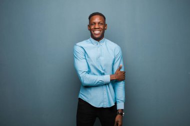 Genç Afro-Amerikan siyahi adam utangaç ve neşeli bir şekilde gülüyor, arkadaş canlısı, olumlu ama güvensiz bir tavırla.