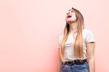 Genç, güzel bir kadın öfkeyle bağırıyor, agresif bağırıyor, gergin ve kızgın görünüyor pembe duvara karşı.