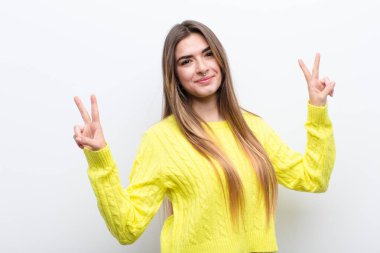 Genç ve güzel bir kadın gülümsüyor ve mutlu görünüyor, arkadaş canlısı ve memnun, işaret eden zafer ya da barış iki elle