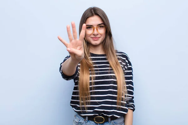 若い女性は笑顔で友好的で前方に手で4番目または4番目を示しソフトブルーの壁に対してカウントダウン — ストック写真