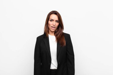 Genç ve güzel iş kadını, kafası karışık ve şaşkın hissediyor, aptal, şaşkın bir yüz ifadesiyle, beyaz duvara karşı beklenmedik bir şeye bakıyor.