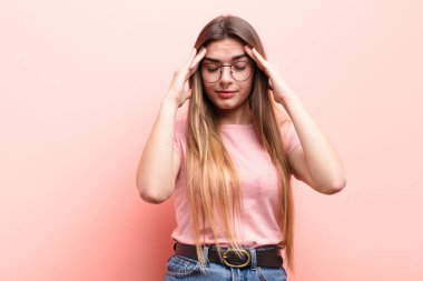 Genç ve güzel bir kadın stresli ve hayal kırıklığına uğramış görünüyor. Baskı altında çalışıyor ve pembe duvara karşı sorunlarla boğuşuyor.