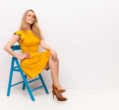 Genç ve güzel sarışın kadın mutlu bir şekilde gülümsüyor. Kalça ve kendine güvenen, pozitif, gururlu ve dost canlısı bir tavırla.