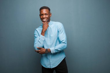 Genç Afro-Amerikan siyahi adam mutlu, kendinden emin bir ifadeyle gülümsüyor. Çenesinde elleri, merak ediyor ve grunge duvarına bakıyor.