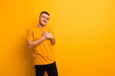 Genç yakışıklı adam romantik, mutlu ve aşık, neşeli bir şekilde gülümseyen ve düz arkaplan karşısında kalbe yakın el ele tutuşan