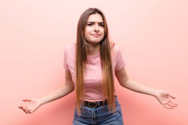 Genç, güzel bir kadın kendini cahil ve şaşkın hissediyor. Hiçbir fikri yok. Pembe duvara karşı aptal ya da aptal bir bakışla kafası karışmış.