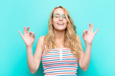 Genç ve güzel sarışın kadın konsantre olmuş ve meditasyon yapıyor, tatmin olmuş ve rahatlamış hissediyor, düşünüyor ya da düz renkli duvara karşı bir seçim yapıyor.