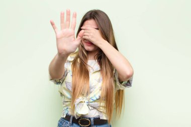 Genç, güzel bir kadın yüzünü eliyle kapatıyor ve kamerayı durdurmak için diğer elini öne koyuyor. Fotoğraf ya da resim çekmeyi reddediyor.