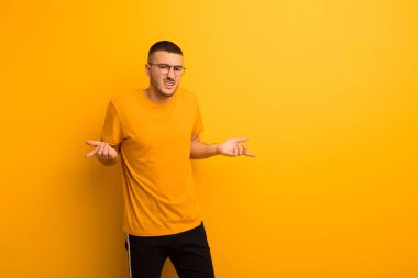 Genç ve yakışıklı bir adam bilgisiz ve kafası karışık, hangi seçeneği seçeceğinden emin değil, düz arkaplanda merak ediyor.