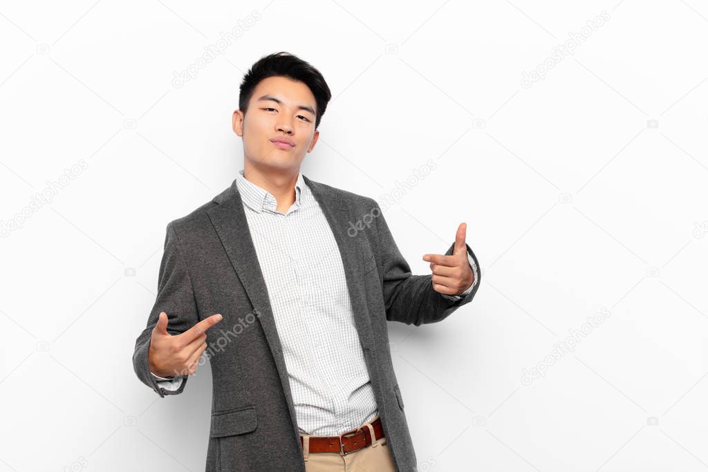 young chinese man looking proud, arrogant, happy, surprised and satisfied, pointing to self, feeling like a winner against flat color wall
