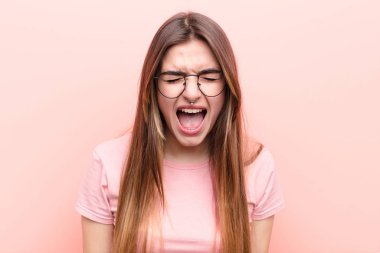 Genç ve güzel bir kadın agresif bir şekilde bağırıyor. Kızgın, sinirli, öfkeli ya da sinirli görünüyor. Pembe duvara karşı hayır diye bağırıyor.