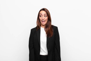 Genç, güzel iş kadını şok olmuş, mutlu, şaşkın ve şaşırmış hissediyor, beyaz duvara karşı ağzı açık bir şekilde yana bakıyor.