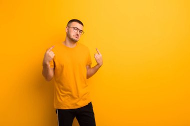 Kötü tavırlı genç yakışıklı adam gururlu ve agresif görünüyor, yukarıyı işaret ediyor ya da düz arkaplan üzerinde ellerle dalga geçiyor.