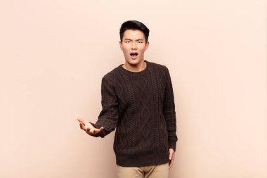 Genç Çinli adam sinirli, sinirli ve hayal kırıklığına uğramış görünüyor. Düz renkli duvara karşı senin neyin var? 