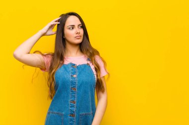 Genç, güzel bir kadın şaşkın ve kafası karışmış hissediyor, başını kaşıyor ve yan tarafa bakıyor.