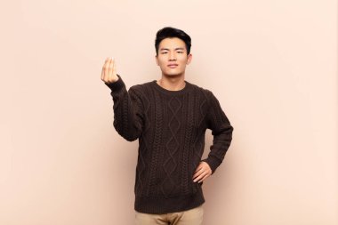 Genç Çinli adam sana borcunu ödemeni söyleyerek kapiş ya da para hareketi yapıyor! yassı renk duvarına karşı