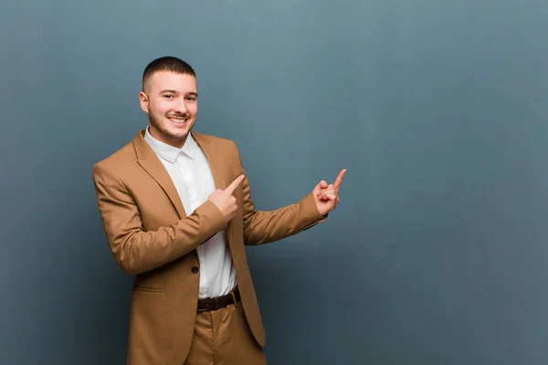young handsome man smiling happily and pointing to side and upwards with both hands showing object in copy space against flat wall