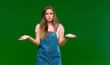 Genç ve güzel bir kadın korkuyla ve ağzı açık bir şekilde yeşil arka planda şaşkın ve şaşkın bir bakışla yukarıya bakıyor.