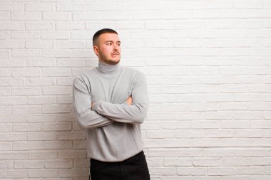 Genç yakışıklı adam şüphe ediyor ya da düşünüyor, dudağını ısırıyor ve kendini güvensiz ve gergin hissediyor, düz arkaplanda boşluğu kopyalamak istiyor.