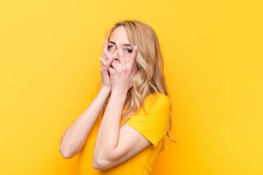 Genç, güzel, sarışın bir kadın korkmuş ya da utanmış hissediyor. Gözleri yarı kapalı, düz renkli duvara bakıyor ya da dikizliyor.