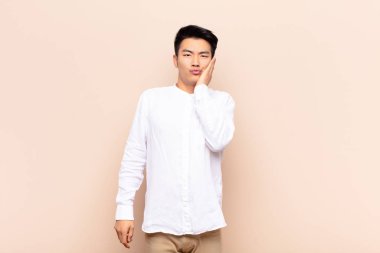 Genç Çinli adam şok olmuş ve şaşkınlık içinde. Düz renkli duvara karşı ağzı sonuna kadar açık inanamıyor.