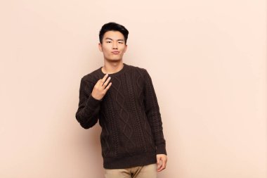 Genç Çinli adam kibirli, başarılı, pozitif ve gururlu görünüyor, düz renkli duvara karşı kendini işaret ediyor.