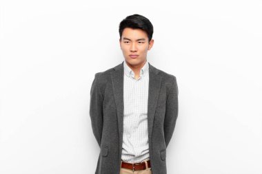 Genç Çinli bir adam üzgün, üzgün ya da kızgın ve olumsuz bir tavır takınıyor, düz renk duvarına karşı anlaşmazlık içinde.