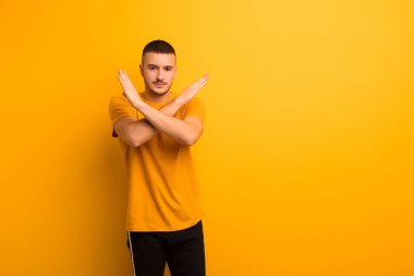 Genç ve yakışıklı adam senin tavırlarından rahatsız ve bıkkın görünüyor, yeter artık! Eller önde çapraz, düz arkaplanda durmanı söylüyor.