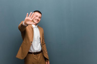 Genç yakışıklı adam gülümsüyor ve arkadaş canlısı görünüyor, 5 ya da 5 numarayı gösteriyor, düz arkaplanda geriye doğru sayıyor.