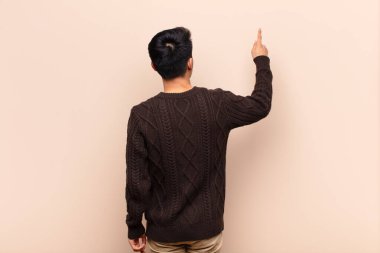 Genç Çinli adam ayakta duruyor ve fotokopi alanındaki objeyi işaret ediyor, düz renkli duvara karşı dikiz manzarası