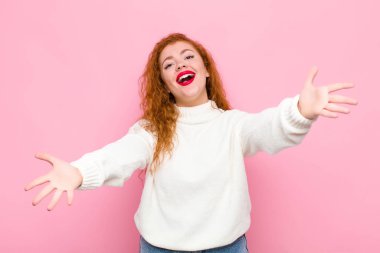 Genç kızıl saçlı kadın neşeyle gülümsüyor sıcak, dostça, sevgi dolu bir kucaklama veriyor, pembe duvara karşı mutlu ve sevimli hissediyor.