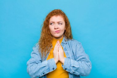 Genç kızıl saçlı kadın gururlu, haylaz ve kibirli hissederken şeytani bir plan kuruyor ya da mavi duvara karşı bir numara düşünüyor.