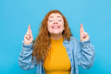 Genç kızıl saçlı kadın gergin ve umutlu, dua ediyor ve mavi duvara karşı iyi şanslar diliyor.