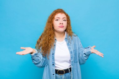 Genç kızıl saçlı kadın şaşkın ve şaşkın hissediyor. Doğru cevap ya da karardan emin değil. Mavi duvara karşı bir seçim yapmaya çalışıyor.