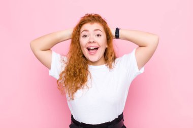 Genç kızıl saçlı kadın mutlu, kaygısız, arkadaş canlısı ve rahat görünüyor. Pembe duvara karşı olumlu bir tavırla hayattan ve başarıdan zevk alıyor.